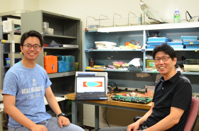 図8.開発中の集積回路の試験の合間に笑顔を見せる戸本教授と山田さん。LHC高輝度化に向けて、KEKエレクトロニクスシステム（E-sys）グループと共同でミューオントリガー回路を開発し、現在は名古屋大学の学生と共同で回路の試験中です。／ © KEK IPNS
